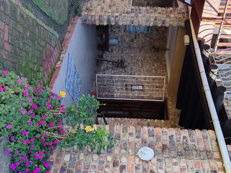 A covered ground-level patio area featuring exposed brickwork, adjacent to a timber staircase and paved garden path.