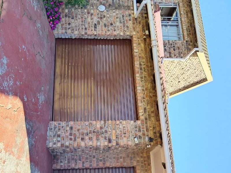 Front view of a double-story brick house featuring a double garage, a balcony, and a paved driveway area.