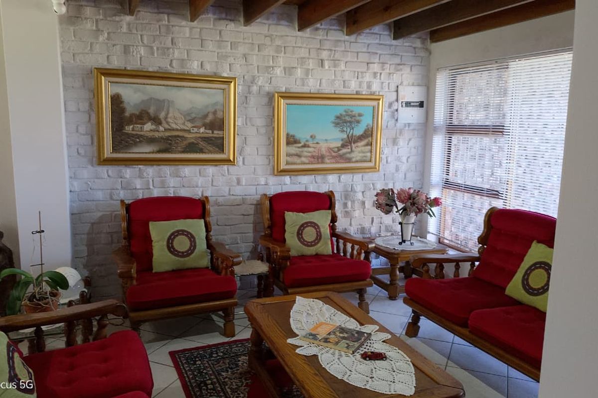 A cozy living room featuring a painted brick feature wall, exposed timber ceiling beams, and large windows that provide natural light.