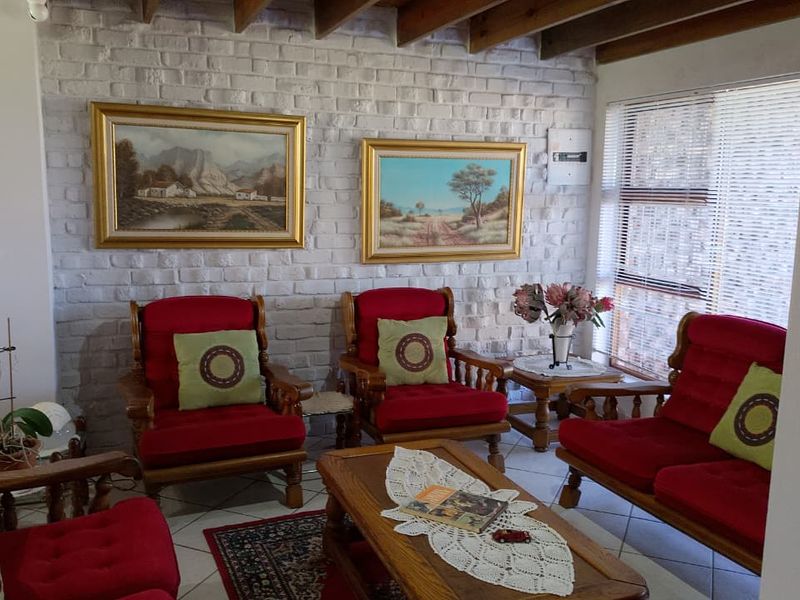 A cozy living room featuring a painted brick feature wall, exposed timber ceiling beams, and large windows that provide natural light.