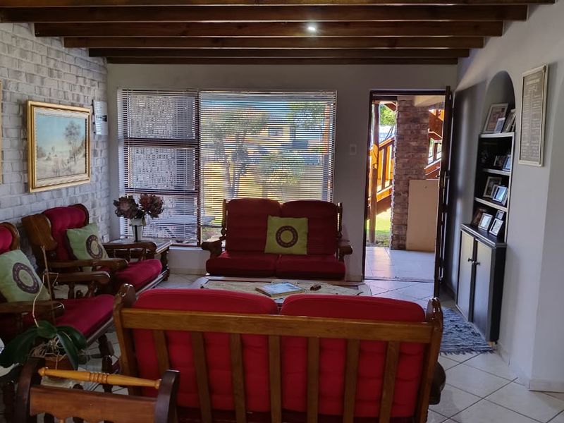 A living room featuring exposed timber ceiling beams, a brick feature wall, tiled flooring, and an arched entryway leading to an outdoor area.