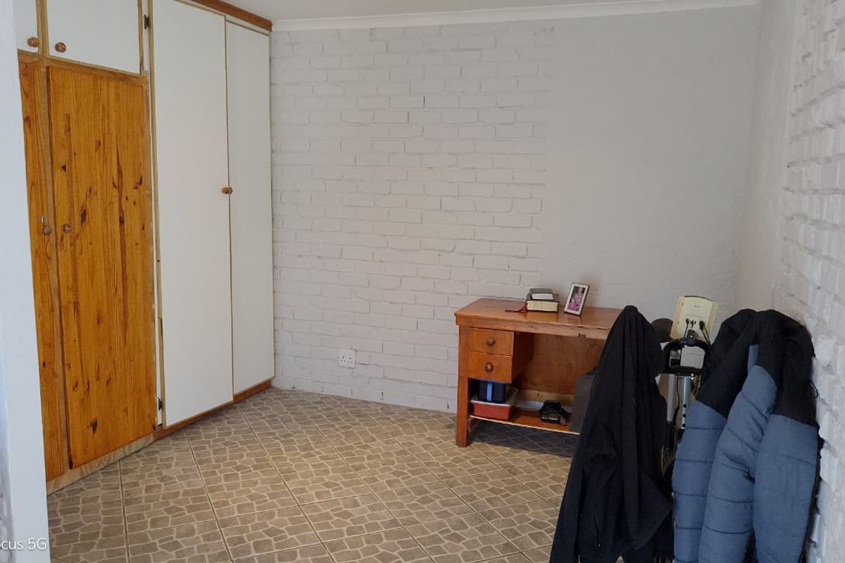 A bedroom featuring built-in cupboards, painted brick walls, and tiled flooring, offering a functional space with potential for modernization.