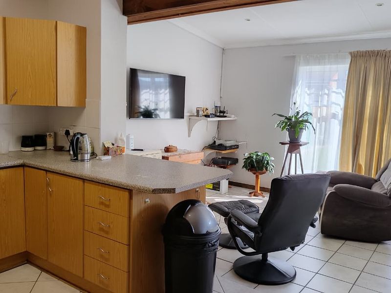Open-plan living area featuring a functional kitchen with laminate cabinetry and tiled flooring, seamlessly connected to a bright lounge space with sliding door access.