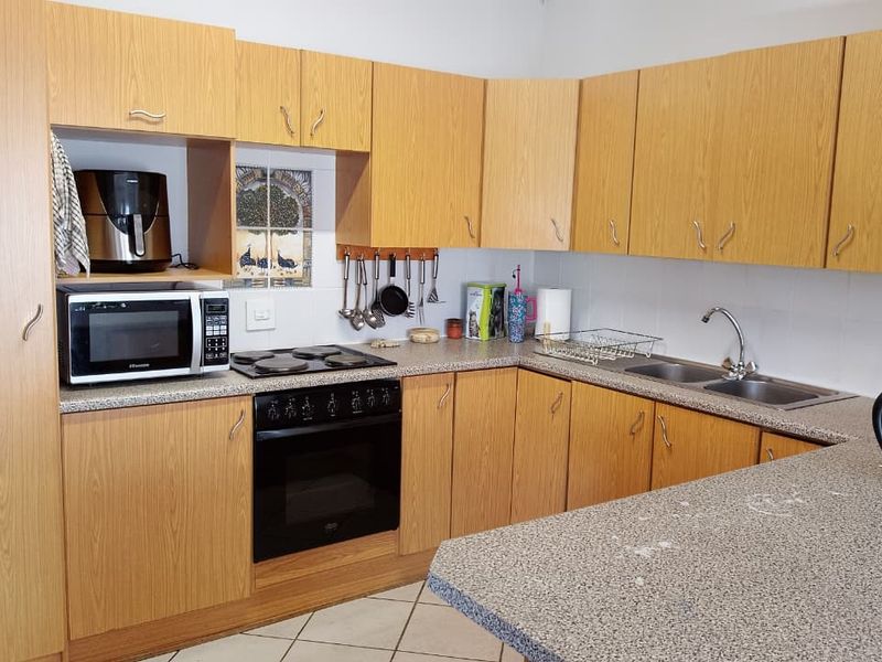 Functional kitchen featuring light wood-look cabinetry, laminate countertops, built-in oven, electric hob, and a double bowl sink with tiled flooring.