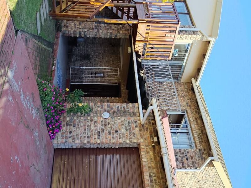 A double-story face brick house featuring a wooden staircase leading to an upper balcony, a single garage, and a paved driveway.