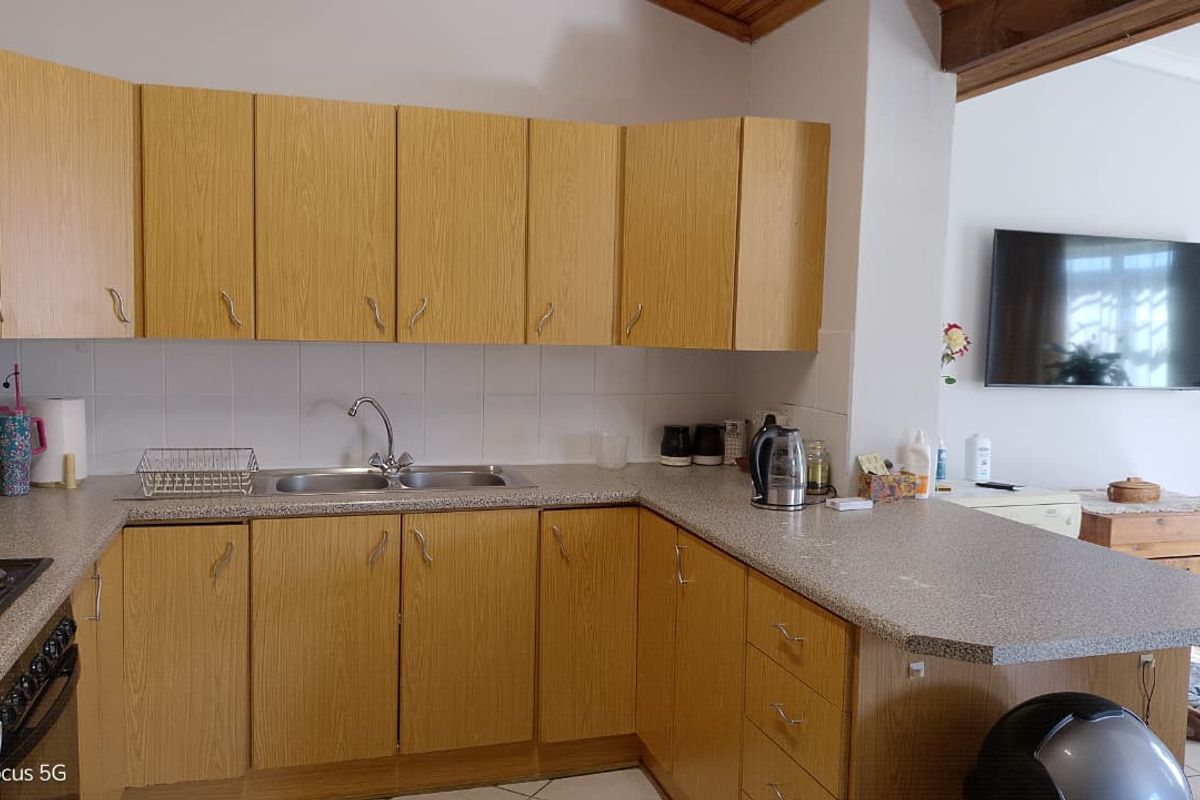 A functional kitchen featuring light wood-look cabinetry, laminate countertops, a double sink, and built-in cooking appliances, complemented by exposed timber ceiling beams.
