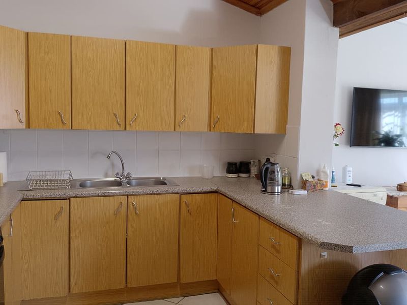 A functional kitchen featuring light wood-look cabinetry, laminate countertops, a double sink, and built-in cooking appliances, complemented by exposed timber ceiling beams.