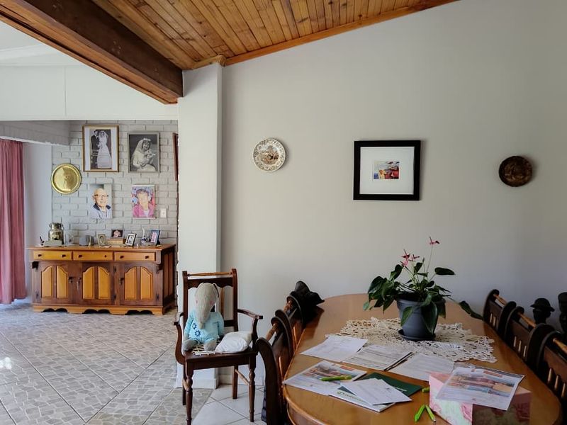 Open plan living and dining area featuring exposed timber ceiling beams, a painted brick feature wall, and tiled flooring.