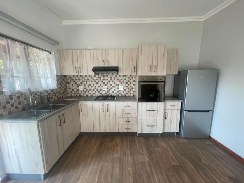 A functional kitchen featuring light wood-look cabinetry, mosaic tile backsplash, built-in oven, gas hob, and durable laminate flooring.