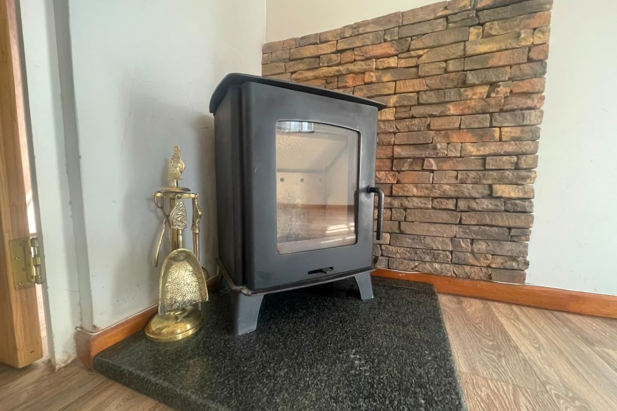 A cozy living room corner featuring a black wood-burning stove set on a granite hearth against a rustic stone veneer feature wall.
