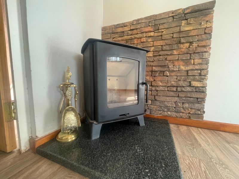 A cozy living room corner featuring a black wood-burning stove set on a granite hearth against a rustic stone veneer feature wall.
