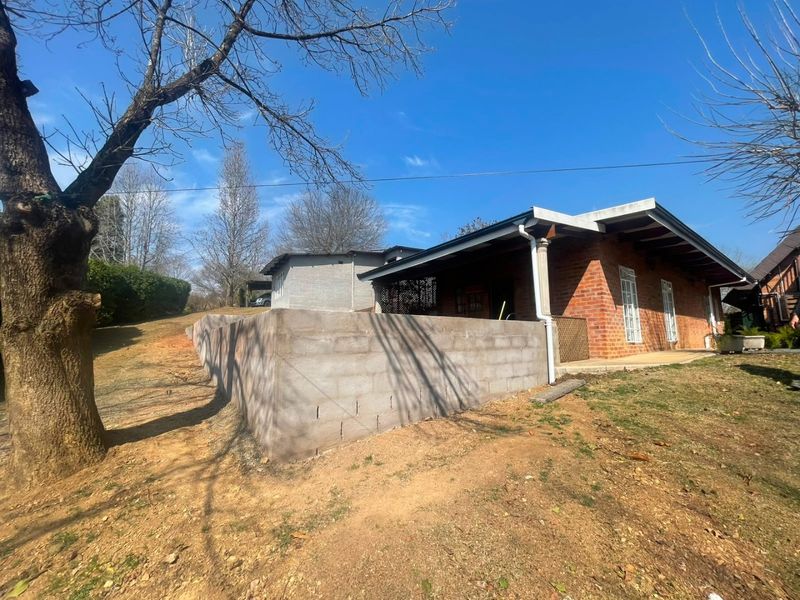 Rear view of the property featuring an exposed brick facade, a covered patio area, and an unfinished concrete block retaining wall in the garden.