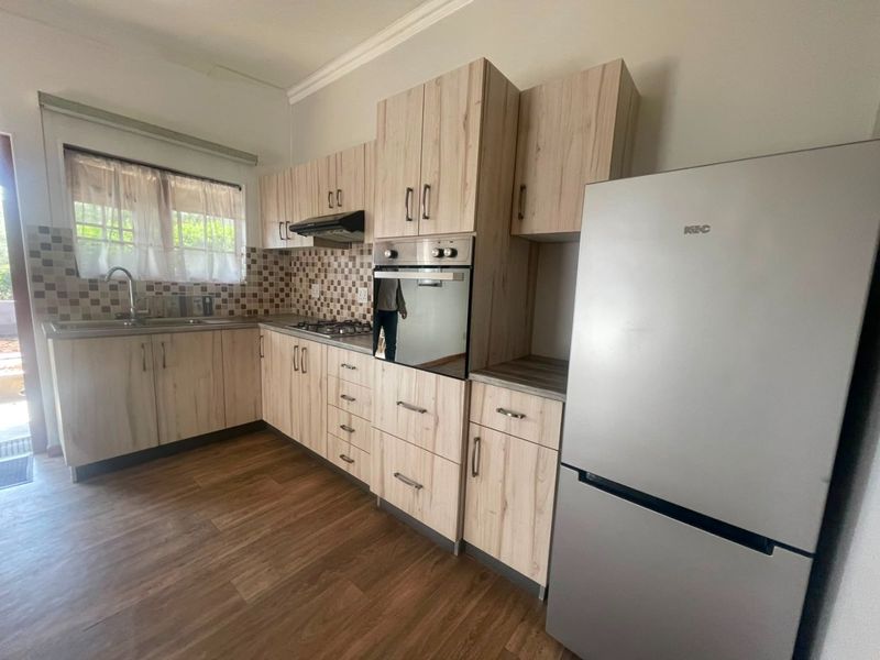 A functional kitchen featuring light wood-grain cabinetry, laminate countertops, a built-in oven with gas hob, and a tiled backsplash.