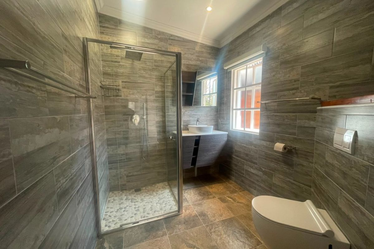 Modern bathroom featuring a glass shower enclosure, wall-mounted vanity with vessel sink, wall-hung toilet with concealed cistern, and contemporary floor-to-ceiling tiling.