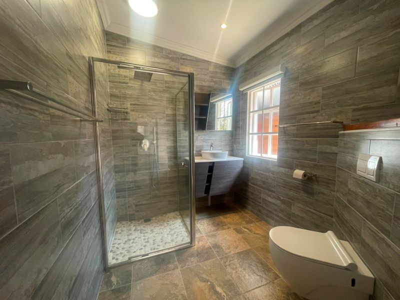 Modern bathroom featuring a glass shower enclosure, wall-mounted vanity with vessel sink, wall-hung toilet with concealed cistern, and contemporary floor-to-ceiling tiling.