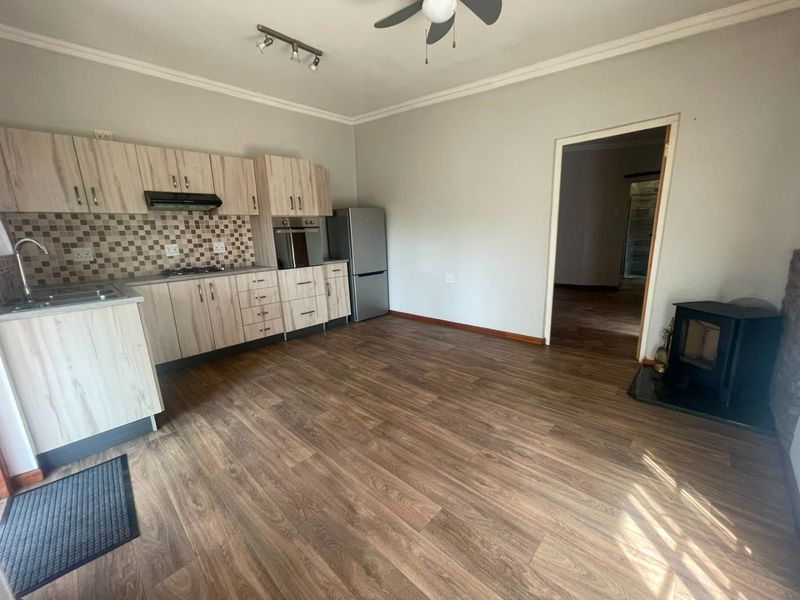 Open-plan kitchen and living area featuring light wood-finish cabinetry, integrated appliances, laminate flooring, and a built-in wood-burning fireplace.