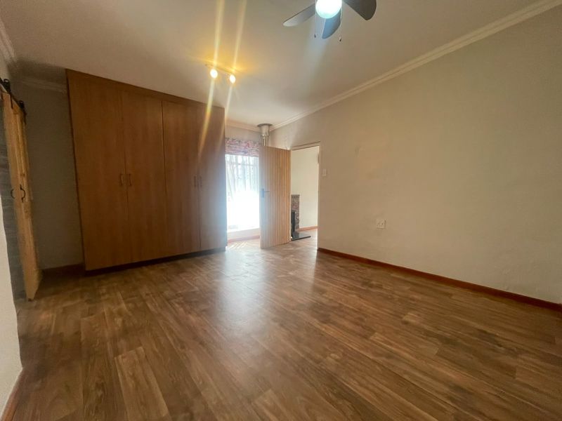 A spacious, empty bedroom featuring wood-look laminate flooring, built-in wooden cupboards, and a ceiling fan, offering a clean canvas for personalization.