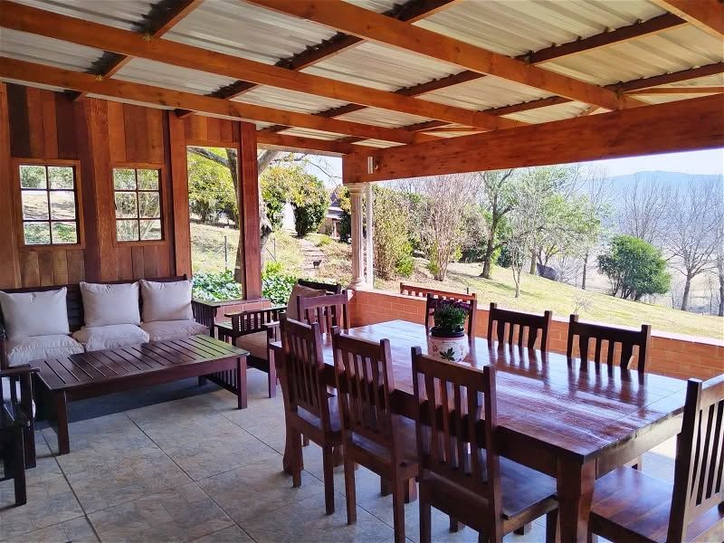 A spacious covered patio featuring timber beam ceilings, wood-paneled walls, and tiled flooring, offering scenic views of the surrounding landscape.