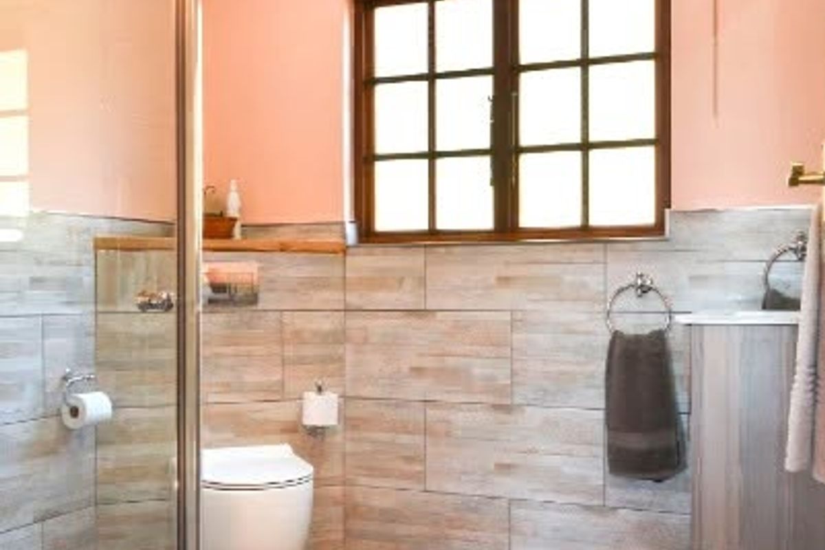 A well-maintained bathroom featuring a glass shower enclosure, timber ceiling, and neutral tiled finishes with a window providing natural light.