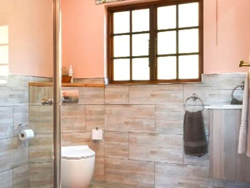A well-maintained bathroom featuring a glass shower enclosure, timber ceiling, and neutral tiled finishes with a window providing natural light.