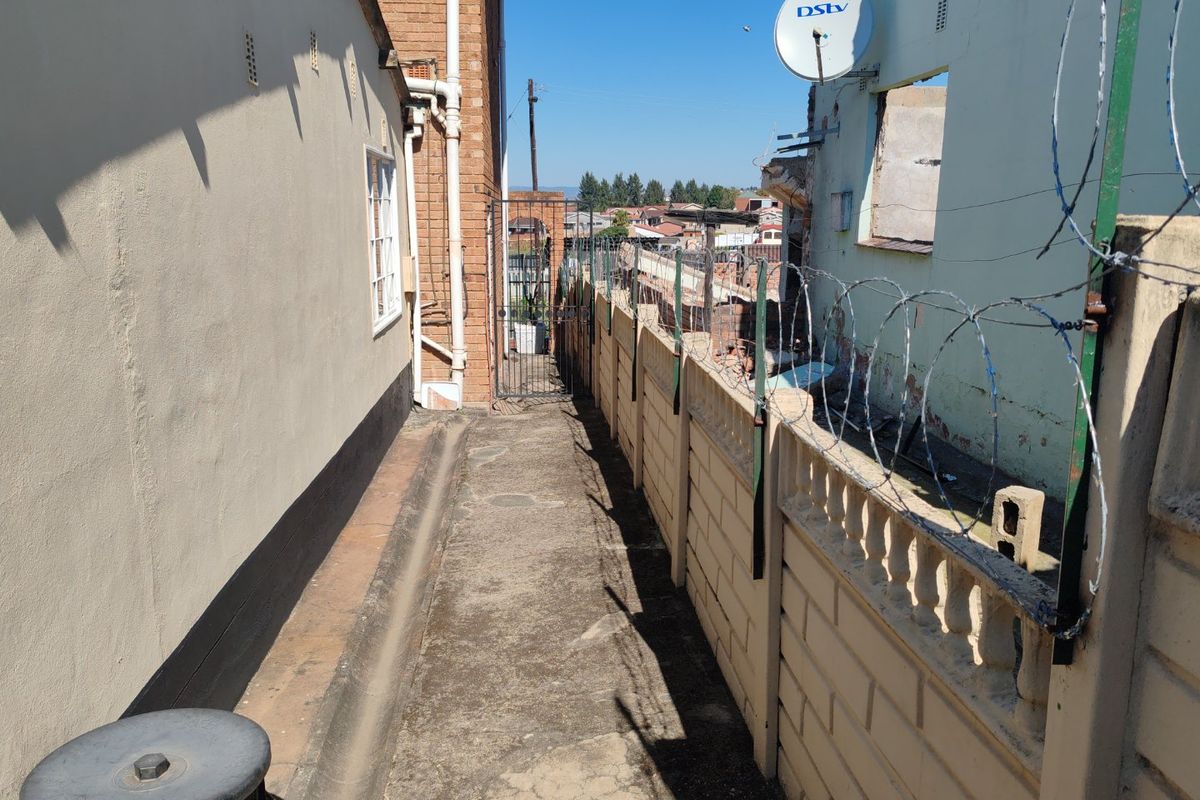 A narrow exterior side passage featuring a precast concrete boundary wall with razor wire and a metal security gate.