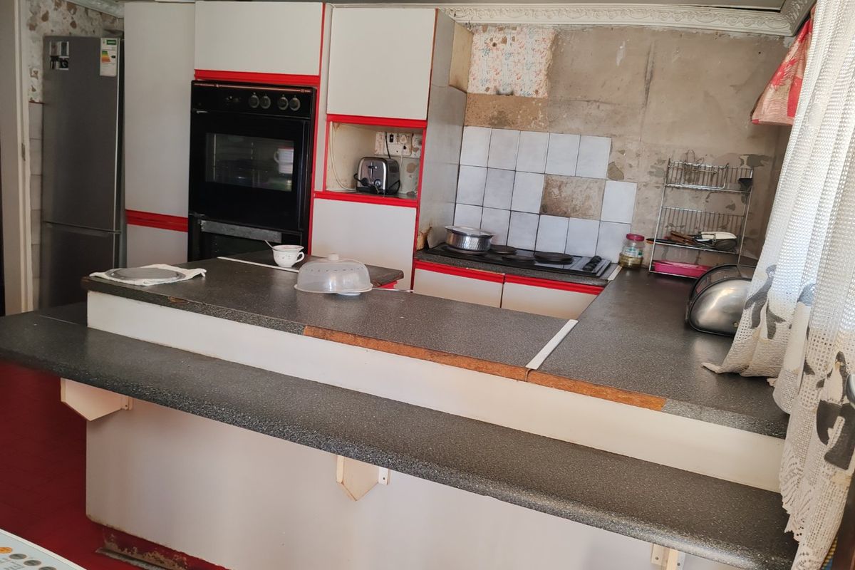 A dated kitchen featuring a breakfast bar, built-in oven, and hob, currently requiring significant renovation to the wall finishes and cabinetry.