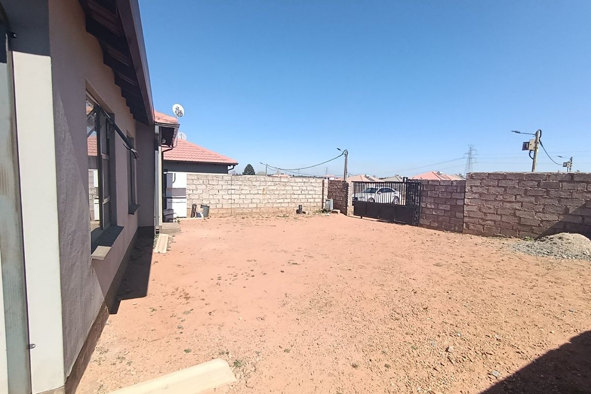 A spacious rear yard featuring a perimeter masonry wall, metal gate, and unlandscaped ground, offering significant potential for garden development and outdoor living space.