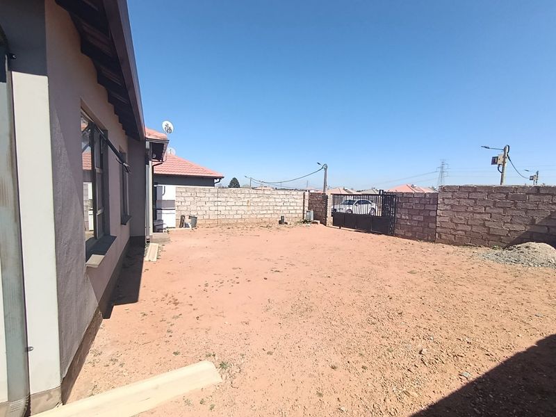 A spacious rear yard featuring a perimeter masonry wall, metal gate, and unlandscaped ground, offering significant potential for garden development and outdoor living space.
