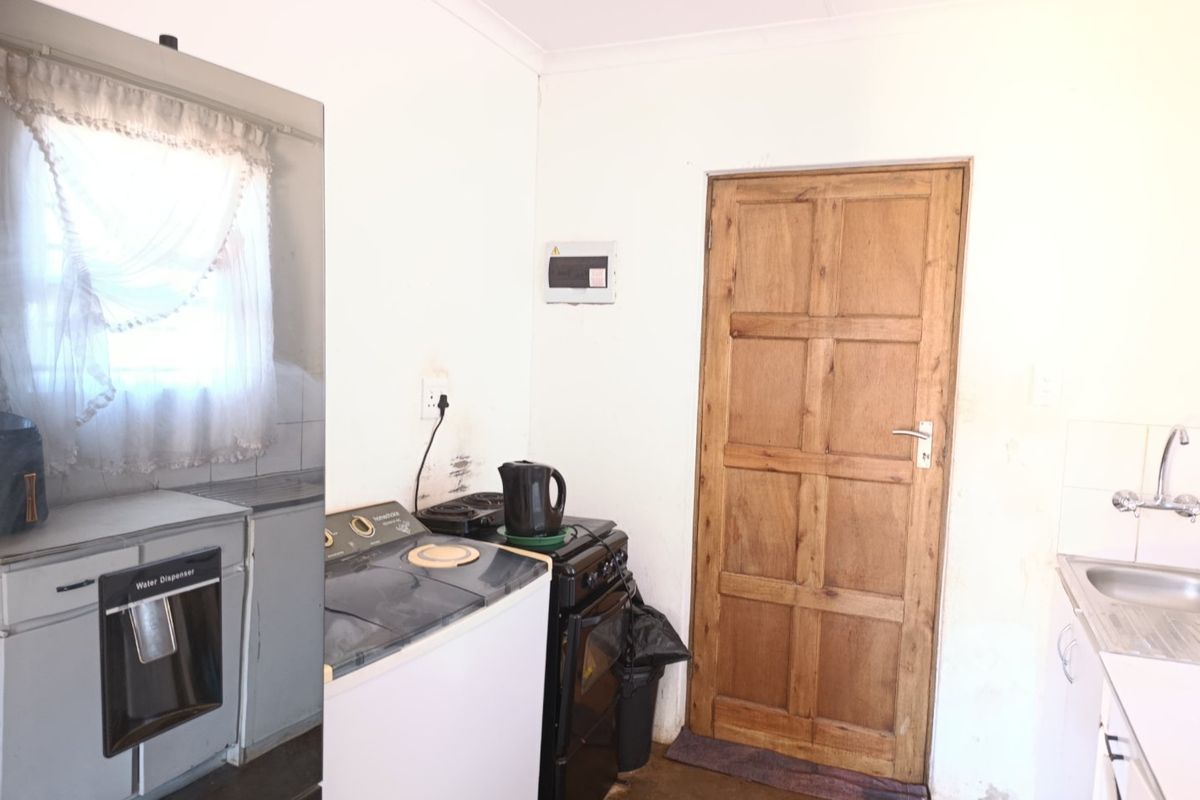 A functional kitchen area featuring a sink, fitted cabinetry, and a wooden door, showing signs of wear and requiring cosmetic updates.