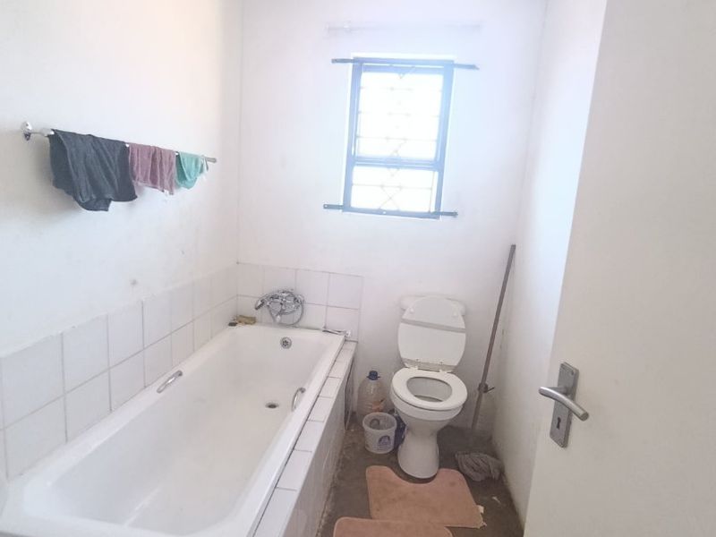 A functional bathroom featuring a built-in bathtub, toilet, and security-barred window, requiring cosmetic updates to improve its overall condition and appeal.