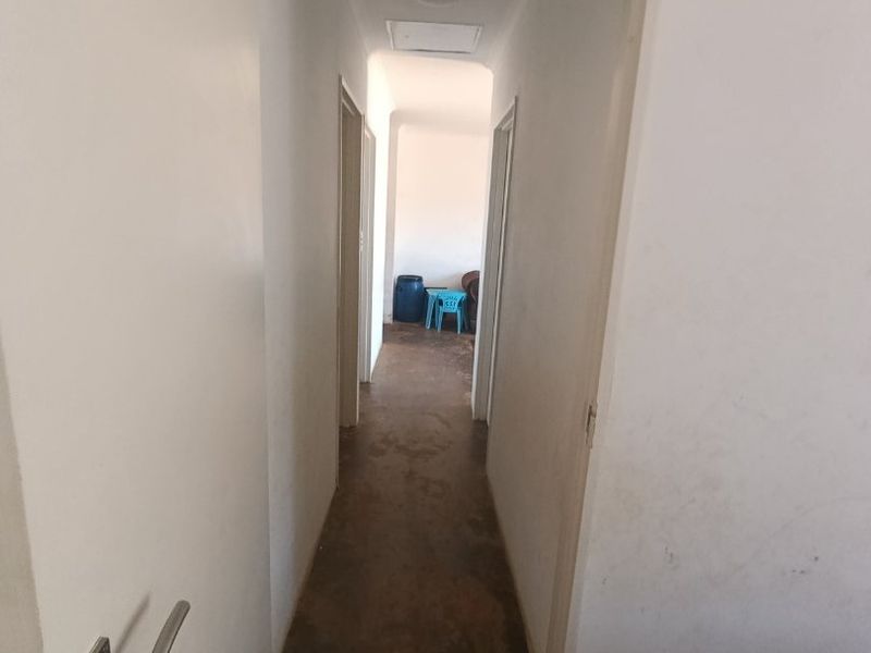 A narrow interior hallway featuring plain white walls and a worn floor surface, providing access to multiple rooms.