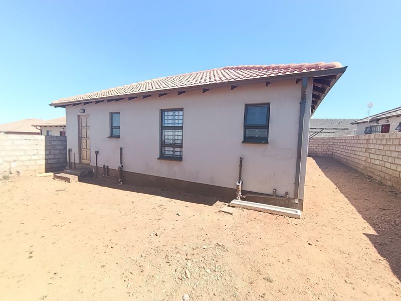Rear view of a single-story house featuring a tiled roof, security bars on windows, and an unlandscaped yard enclosed by concrete boundary walls.