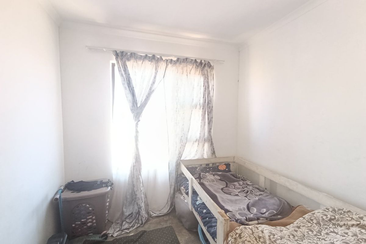 A compact bedroom featuring plain white walls and a window with a curtain rod, requiring cosmetic updates to improve its overall appeal.