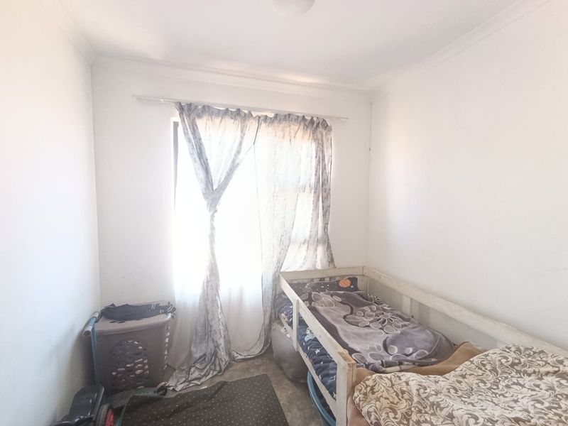 A compact bedroom featuring plain white walls and a window with a curtain rod, requiring cosmetic updates to improve its overall appeal.