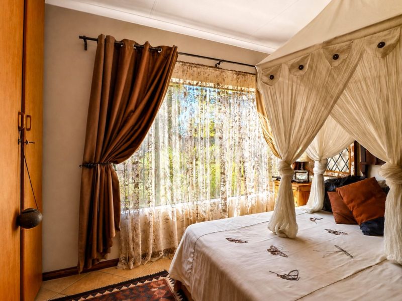 A bedroom featuring tiled flooring, a built-in wardrobe, and a large window with curtain fixtures, offering a functional and comfortable living space.