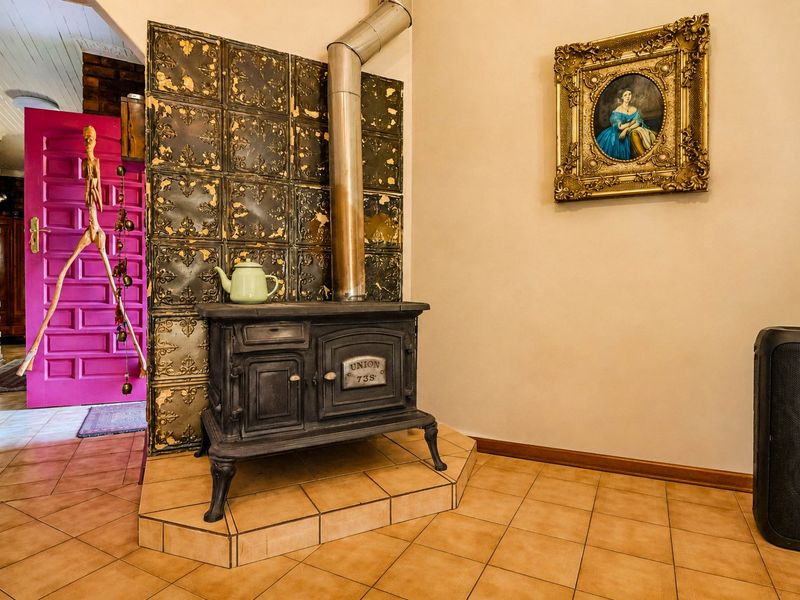 Living area featuring a vintage cast iron wood burning stove set on a tiled hearth with decorative metal wall cladding and ceramic flooring.