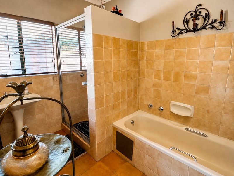 A functional bathroom featuring a built-in bathtub, separate shower enclosure, and pedestal sink with neutral tiled finishes throughout.