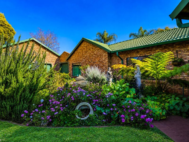 Front elevation of a face brick house featuring a green tiled roof and a well-established landscaped garden with a paved walkway.