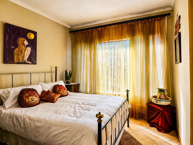 A cozy bedroom featuring tiled flooring and a large window dressed with sheer curtains, providing natural light to the space.