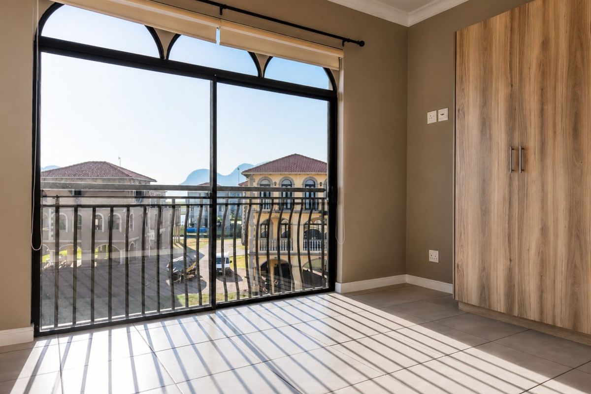 A bright, empty bedroom featuring tiled floors, a built-in wooden wardrobe, and a large sliding glass door opening to a balcony with neighborhood views.