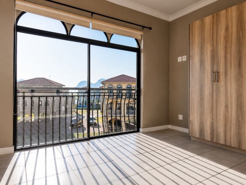 A bright, empty bedroom featuring tiled floors, a built-in wooden wardrobe, and a large sliding glass door opening to a balcony with neighborhood views.