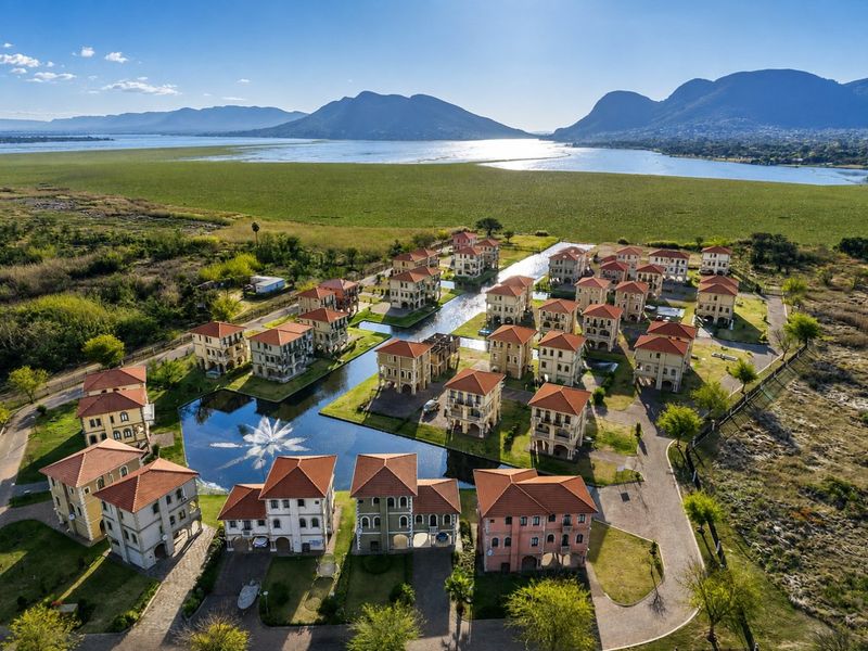 Aerial view of a residential estate featuring multiple multi-story homes, paved driveways, and a central water feature set against a scenic lake and mountain backdrop.