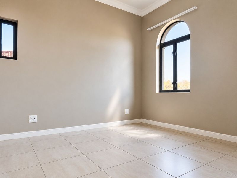 A bright, empty bedroom featuring neutral walls, tiled flooring, and a distinctive arched window, providing a clean canvas for interior design.