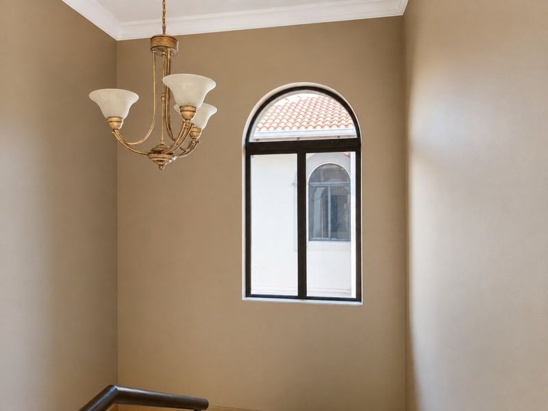 A bright hallway area featuring an elegant arched window, crown molding, and a classic chandelier, providing a clean and well-maintained transition space.