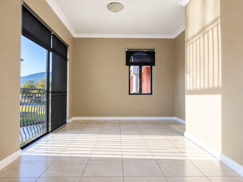 A bright, empty living area featuring neutral tiled flooring, an arched window, and a large sliding glass door leading to an outdoor balcony.