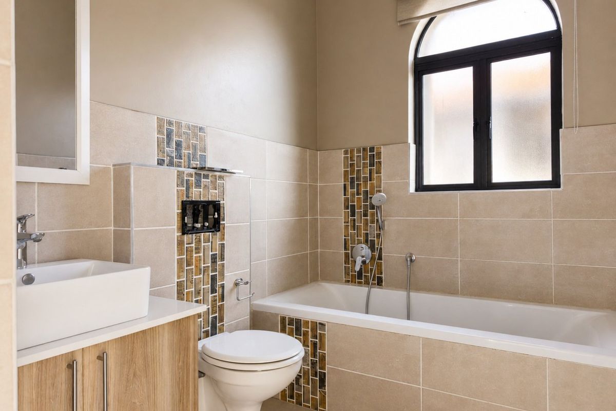 Modern bathroom featuring a wall-mounted toilet, built-in bathtub with mosaic tile accents, vanity cabinet with vessel sink, and an arched window.