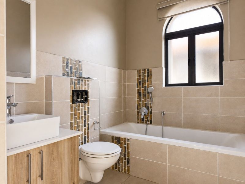 Modern bathroom featuring a wall-mounted toilet, built-in bathtub with mosaic tile accents, vanity cabinet with vessel sink, and an arched window.