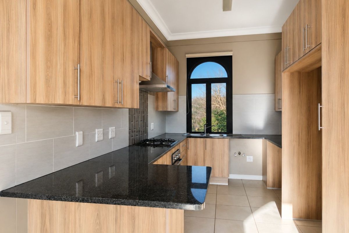 Modern kitchen featuring light wood cabinetry, black granite countertops, built-in gas hob, oven, extractor fan, and tiled finishes with an arched window.