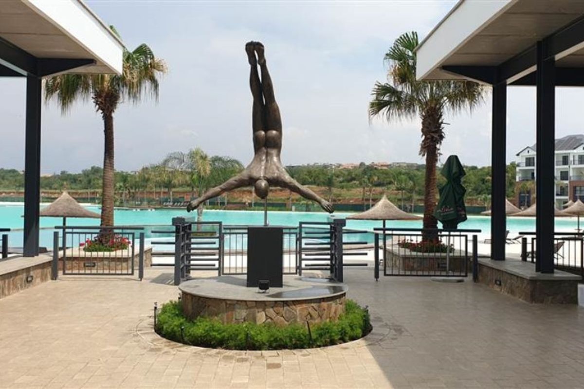 A well-maintained outdoor pool area featuring a central sculpture, stone-clad pedestal, and covered walkways overlooking a large swimming pool.