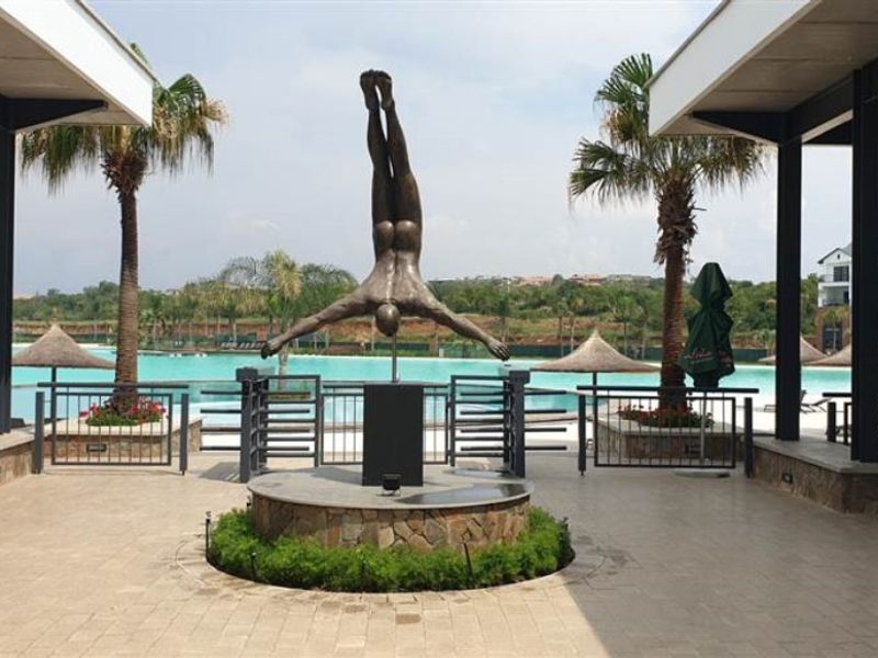 A well-maintained outdoor pool area featuring a central sculpture, stone-clad pedestal, and covered walkways overlooking a large swimming pool.